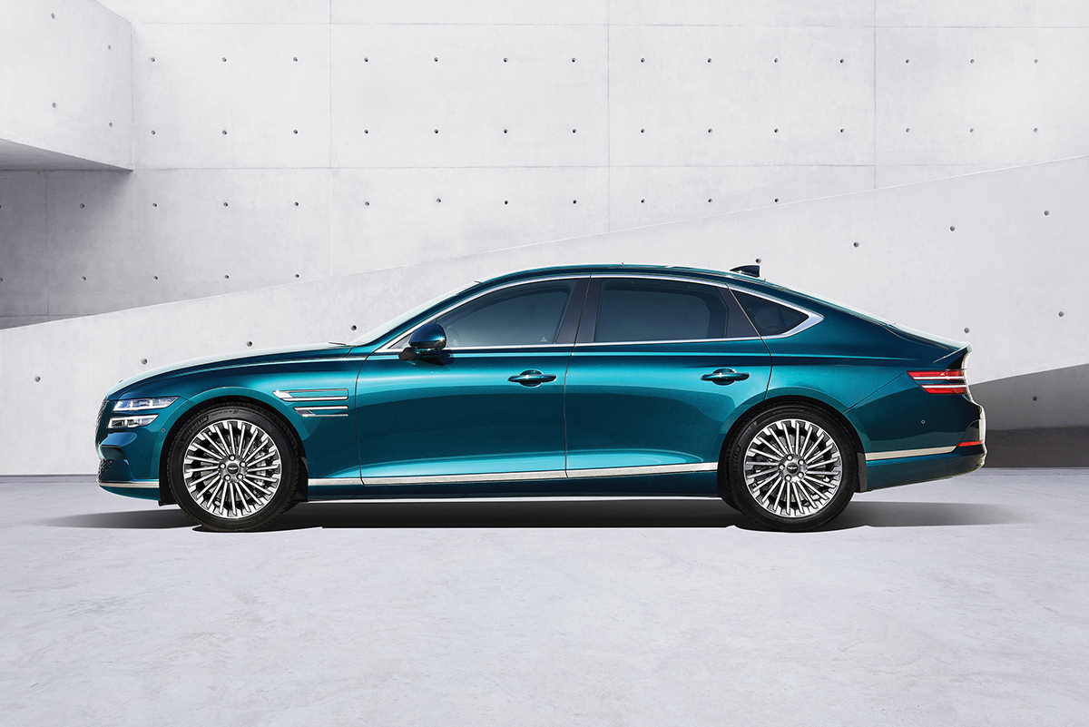 Side view of turquoise Genesis G80 in front of light cement wall with small hole pattern